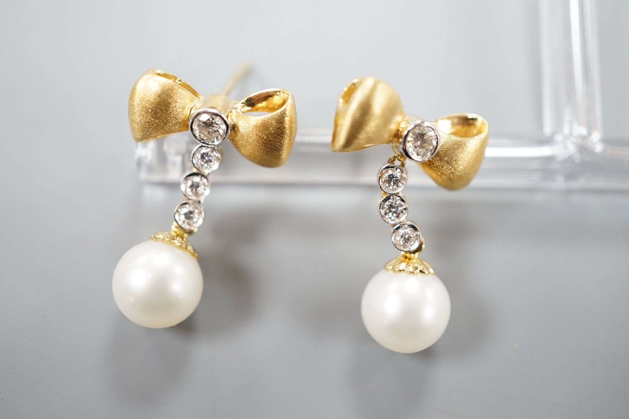 A modern pair of 750 yellow metal, cultured pearl and diamond set ribbon bow drop earrings